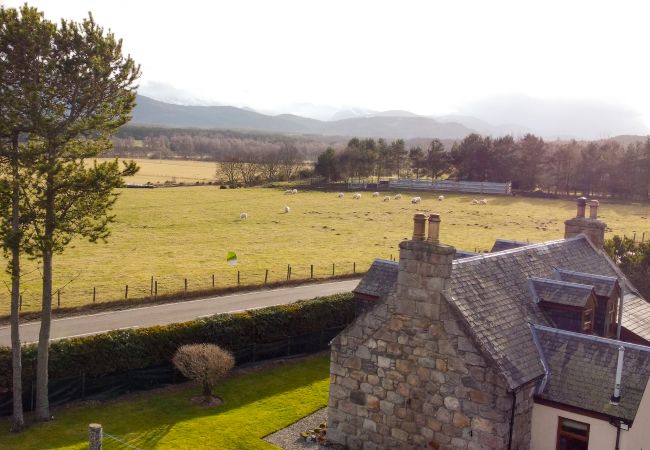 Pilmuir Cottage exterior looking across towards Cairngorms, mountains in distance and sheep in nearby field