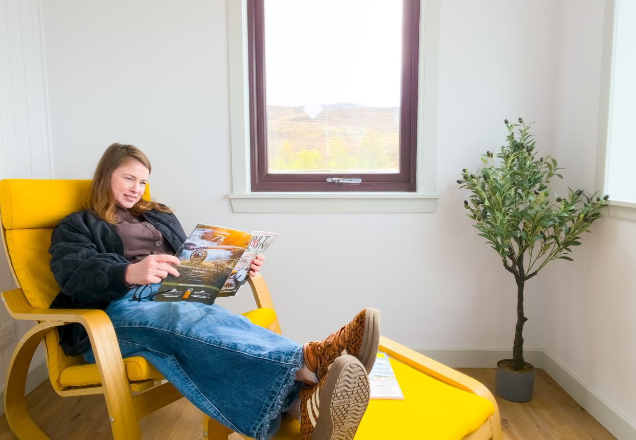 Guest relaxing in yellow reading chair with a book by the window at Lynemore Croft