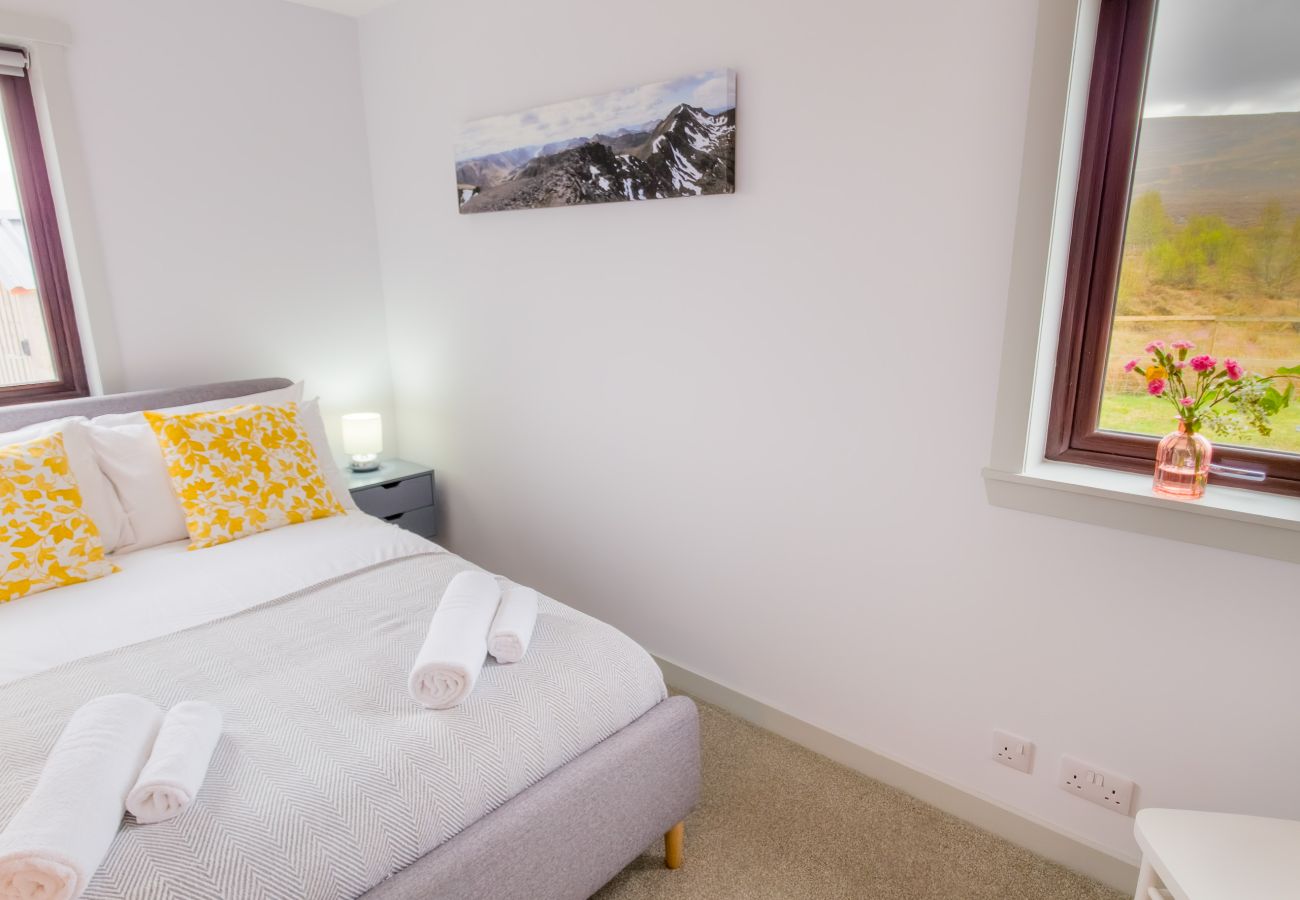 Double bedroom with grey upholstered bed, yellow cushions and Highland print at Lynemore Croft