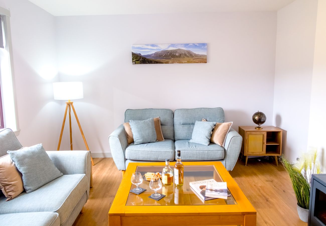Airy living room with grey sofas, whisky on coffee table and Highland mountain print at Lynemore Croft