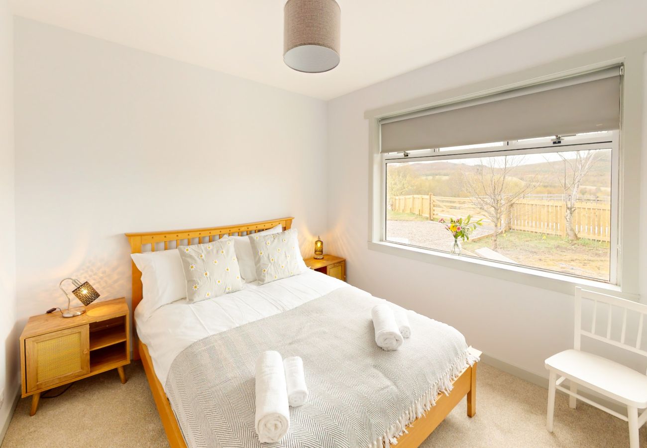 Bright double bedroom with wooden bed frame and garden window at Lynemore Croft