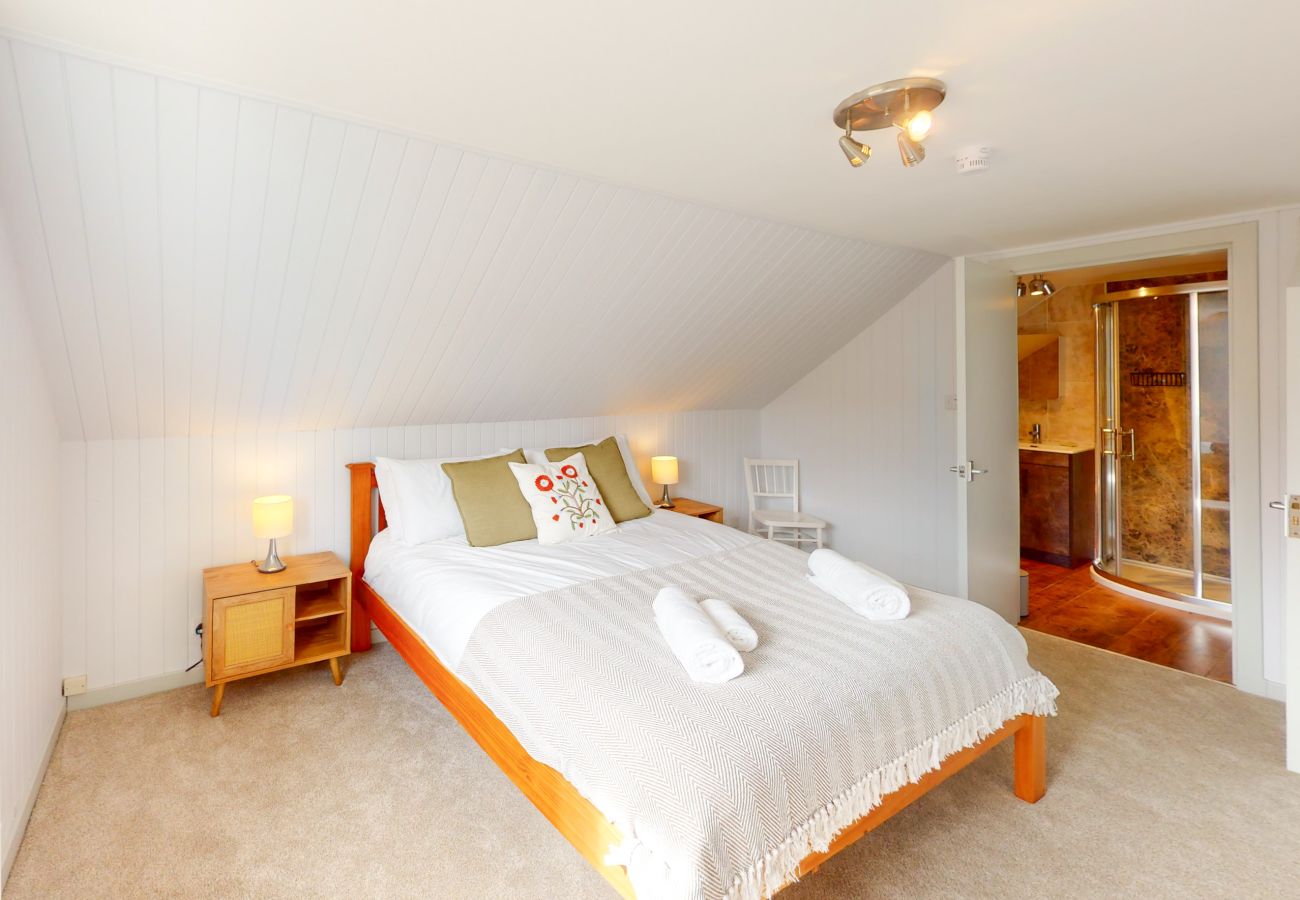 Double bedroom with vaulted ceiling, wooden bed frame and green cushions at Lynemore Croft