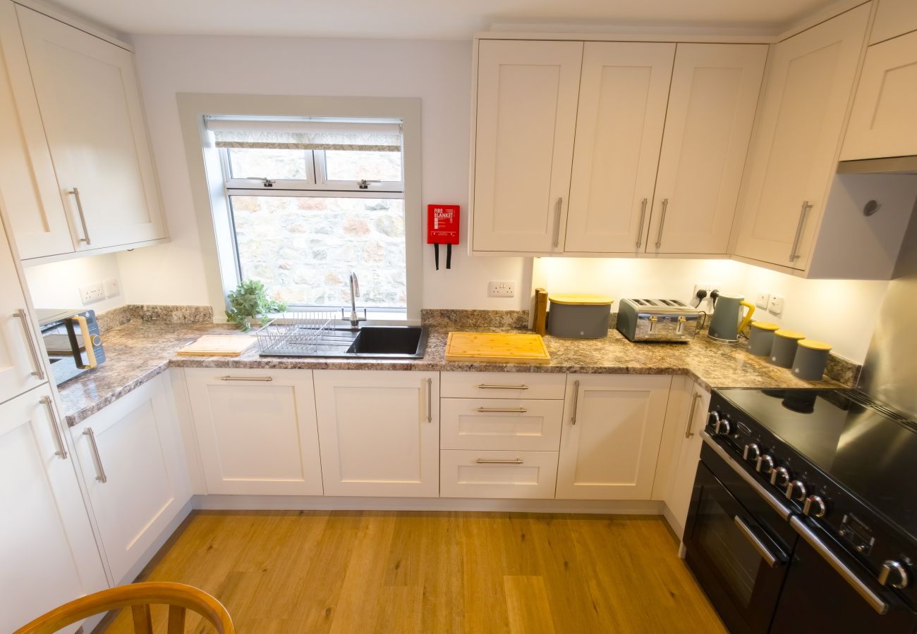 Clean white kitchen with granite worktops and built-in appliances at Lynemore Croft