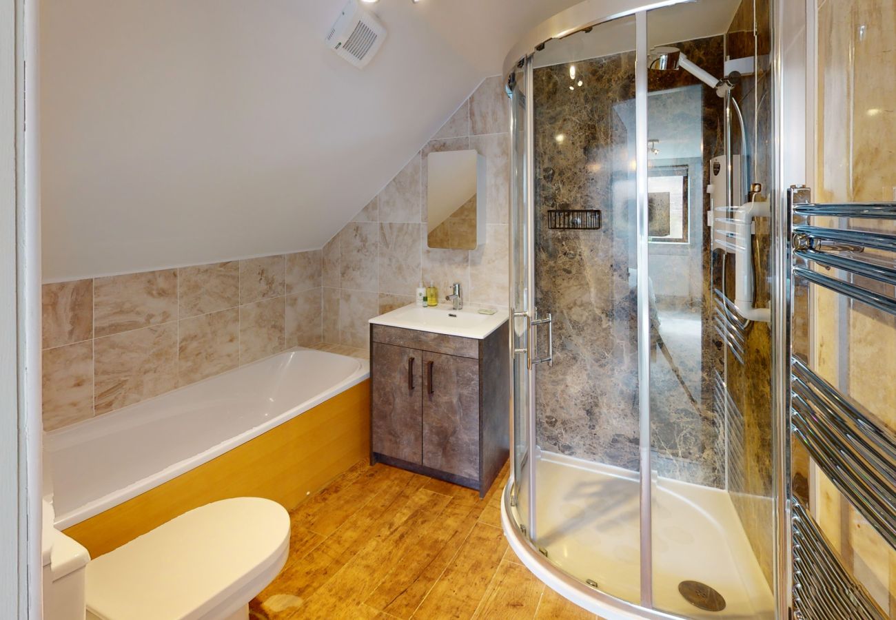 Bathroom with full bath, corner shower enclosure and wooden floor at Lynemore Croft