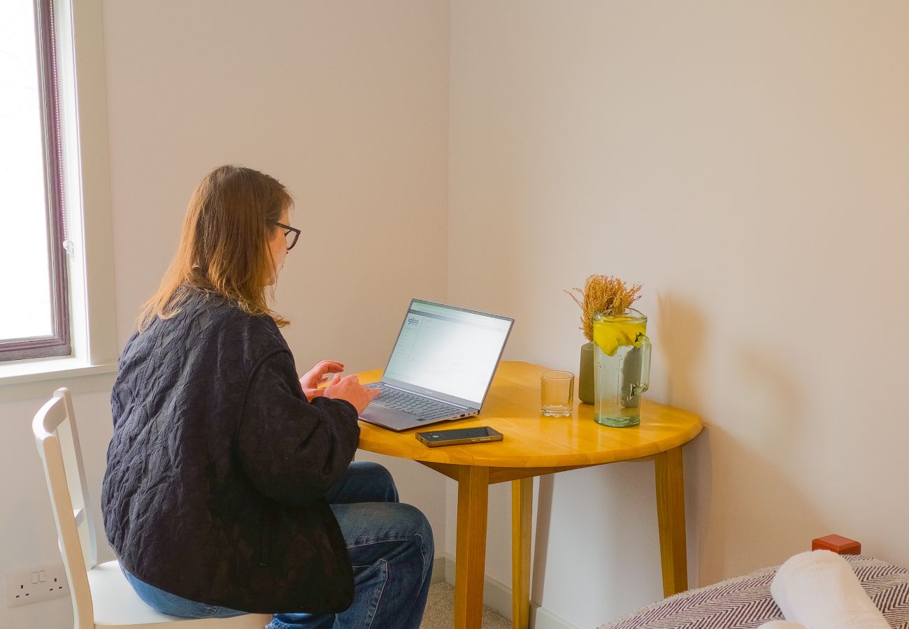 Person working on laptop at wooden desk in bedroom at Lynemore Croft