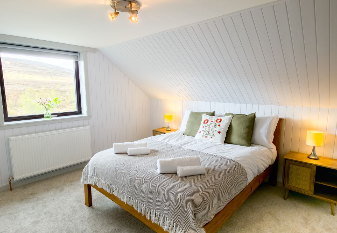 Bright bedroom with sloped ceiling, green cushions and Highland moorland views at Lynemore Croft