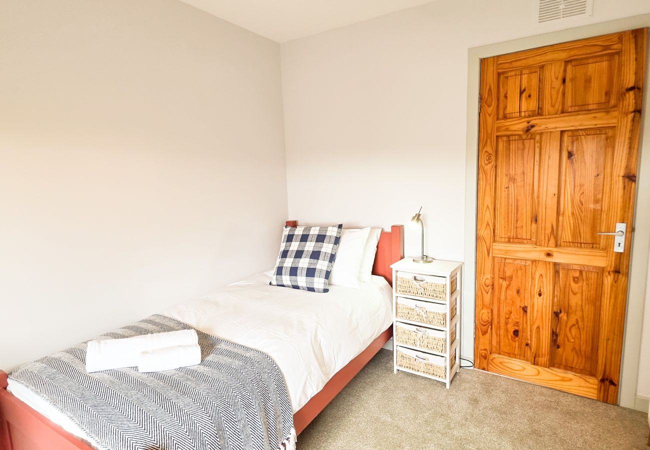 Bedroom with coral bed frame, pine door and checked blue pillow at Lynemore Croft