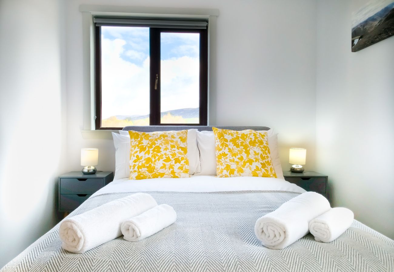 Double bedroom with yellow floral cushions, dark bedside tables and Highland sky window view at Lynemore Croft