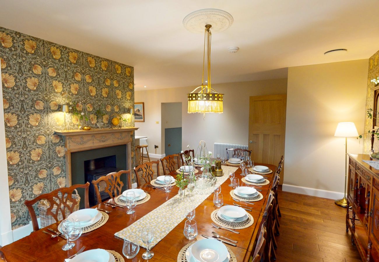 Elegant dining room with long table, chandelier and Arts and Crafts wallpaper at Lynwilg House