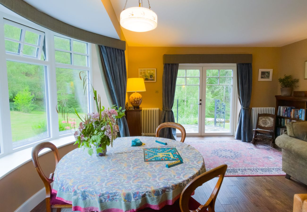 Bright sitting area with wrap-around windows and green garden views at Lynwilg House Highland holiday