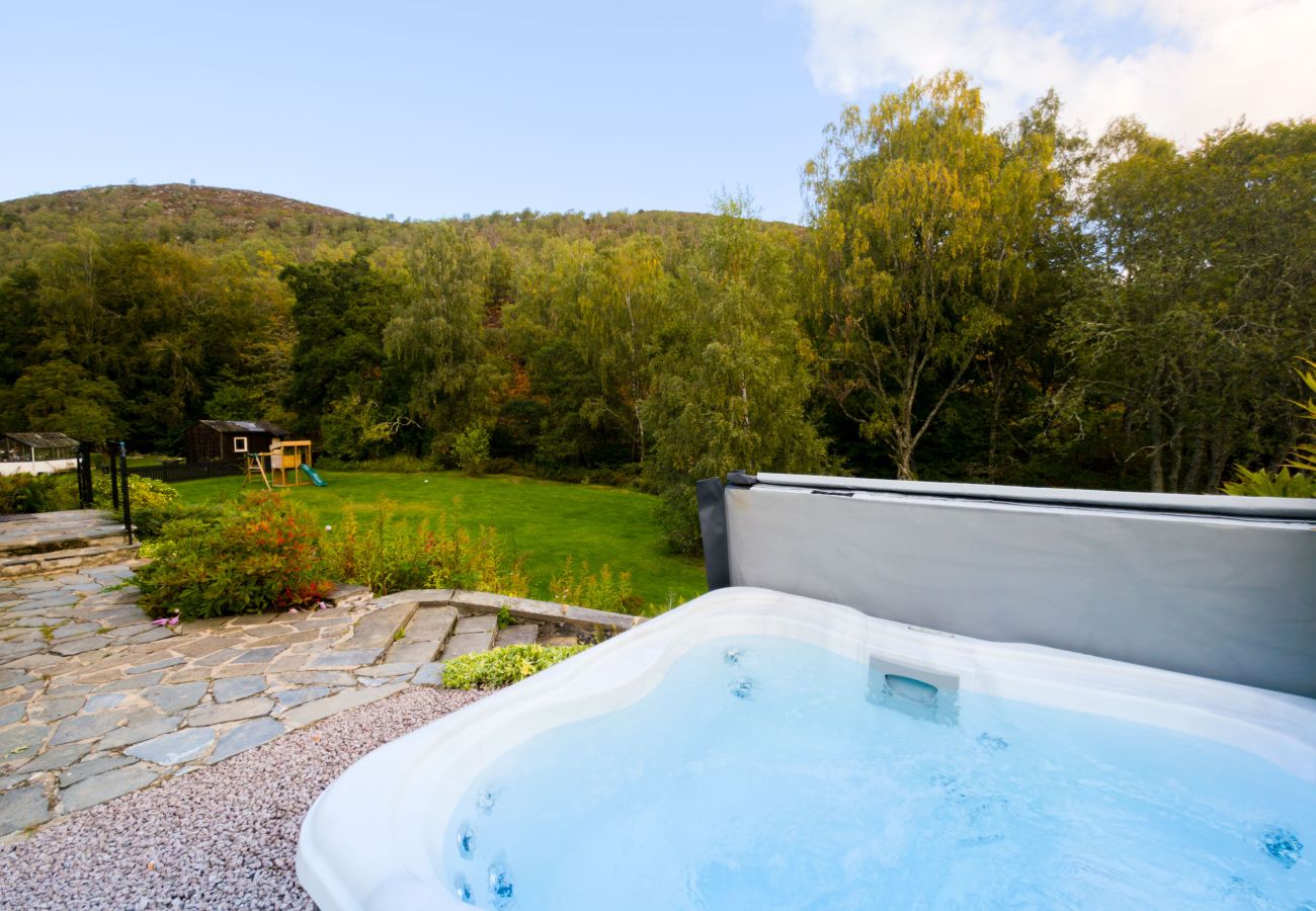 Close-up of the bubbling hot tub with lawn, stone paths and woodland beyond at Lynwilg House
