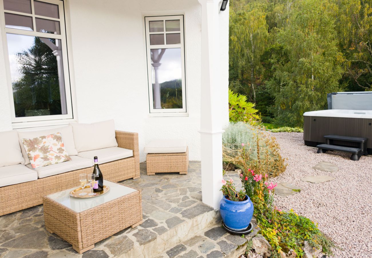 Rattan sofa and coffee table on a covered veranda, with the hot tub beyond on the gravel terrace at Lynwilg House