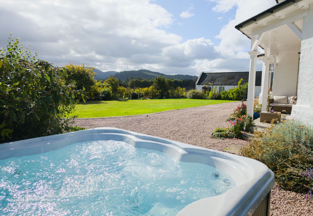 Bubbling hot tub beside the gravel drive and veranda, with a large lawn and hills beyond at Lynwilg House