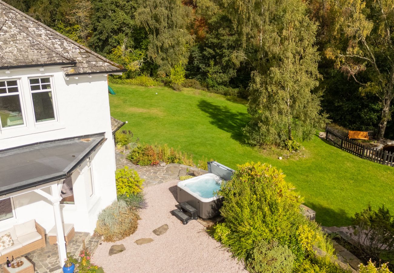 Hot tub on a gravel terrace beside the house and veranda, with lawn and mature trees at Lynwilg House