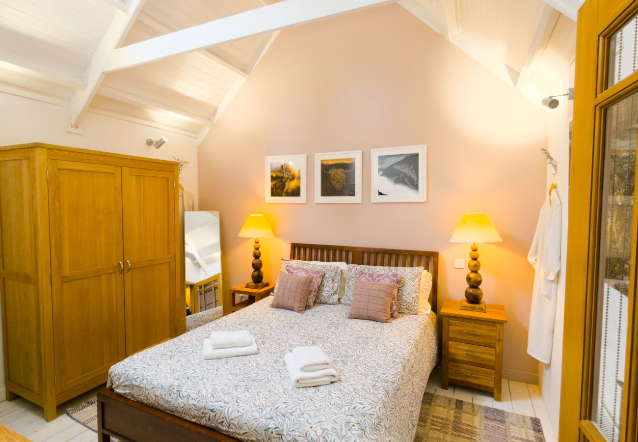 Double bed with wooden headboard, bedside lamps and pine wardrobe in the bedroom at Wildcat Lodge, Boat of Garten