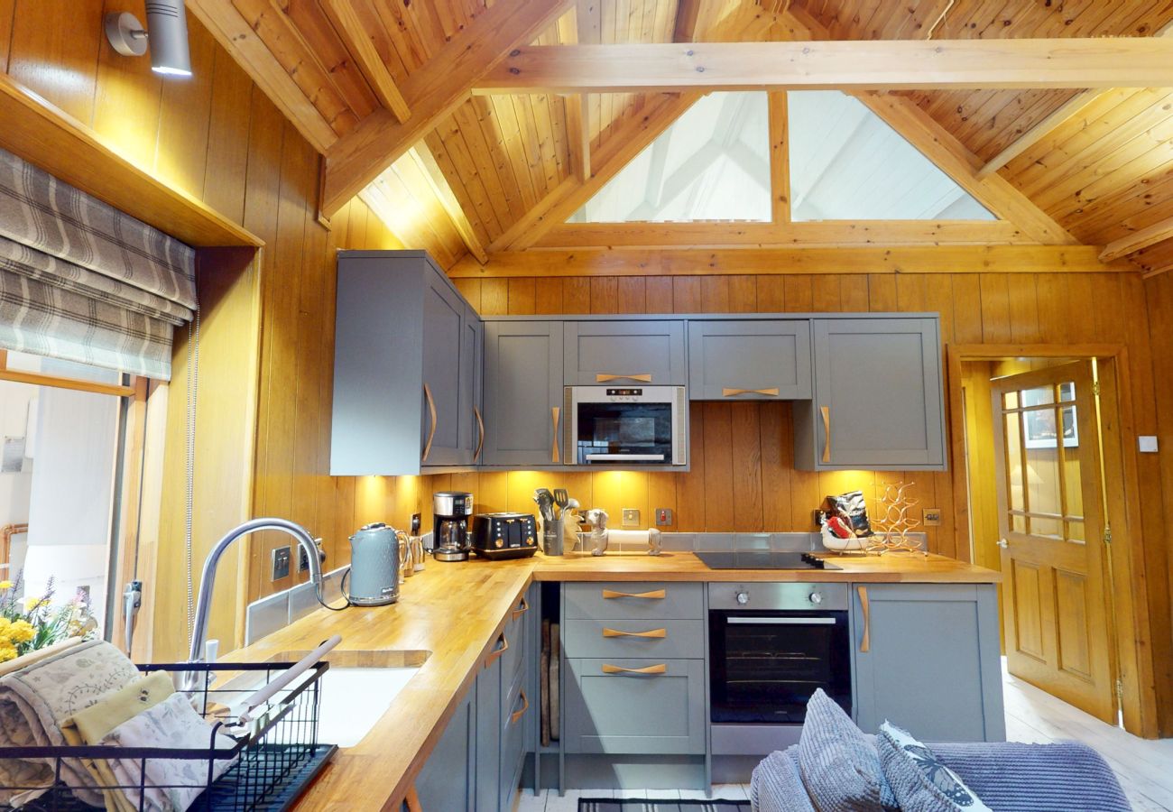Wooden worktop, sink and grey kitchen units under a pitched pine ceiling at Wildcat Lodge, Cairngorms