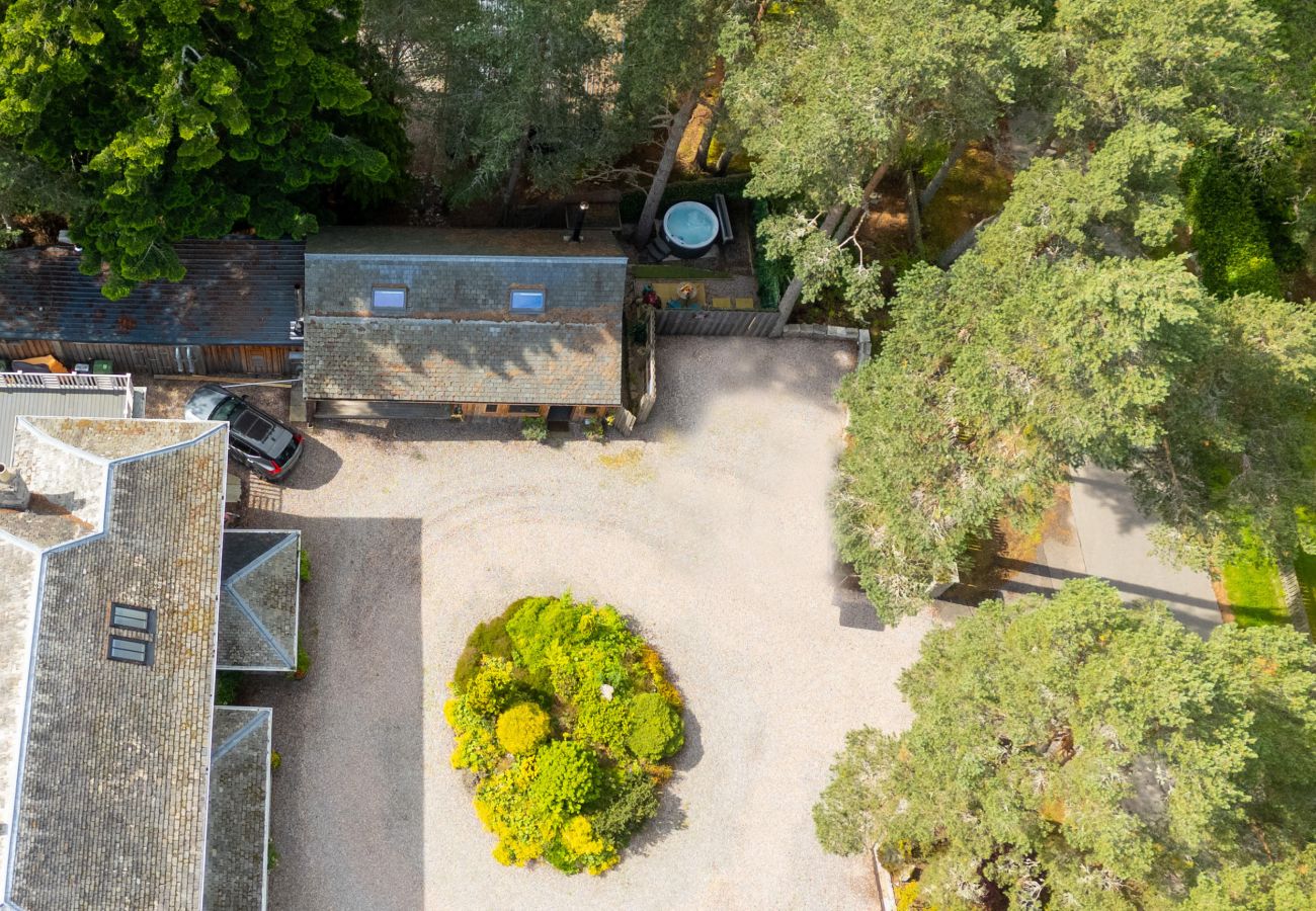 Aerial view of Wildcat Lodge among mature trees with gravel parking and hot tub, Boat of Garten