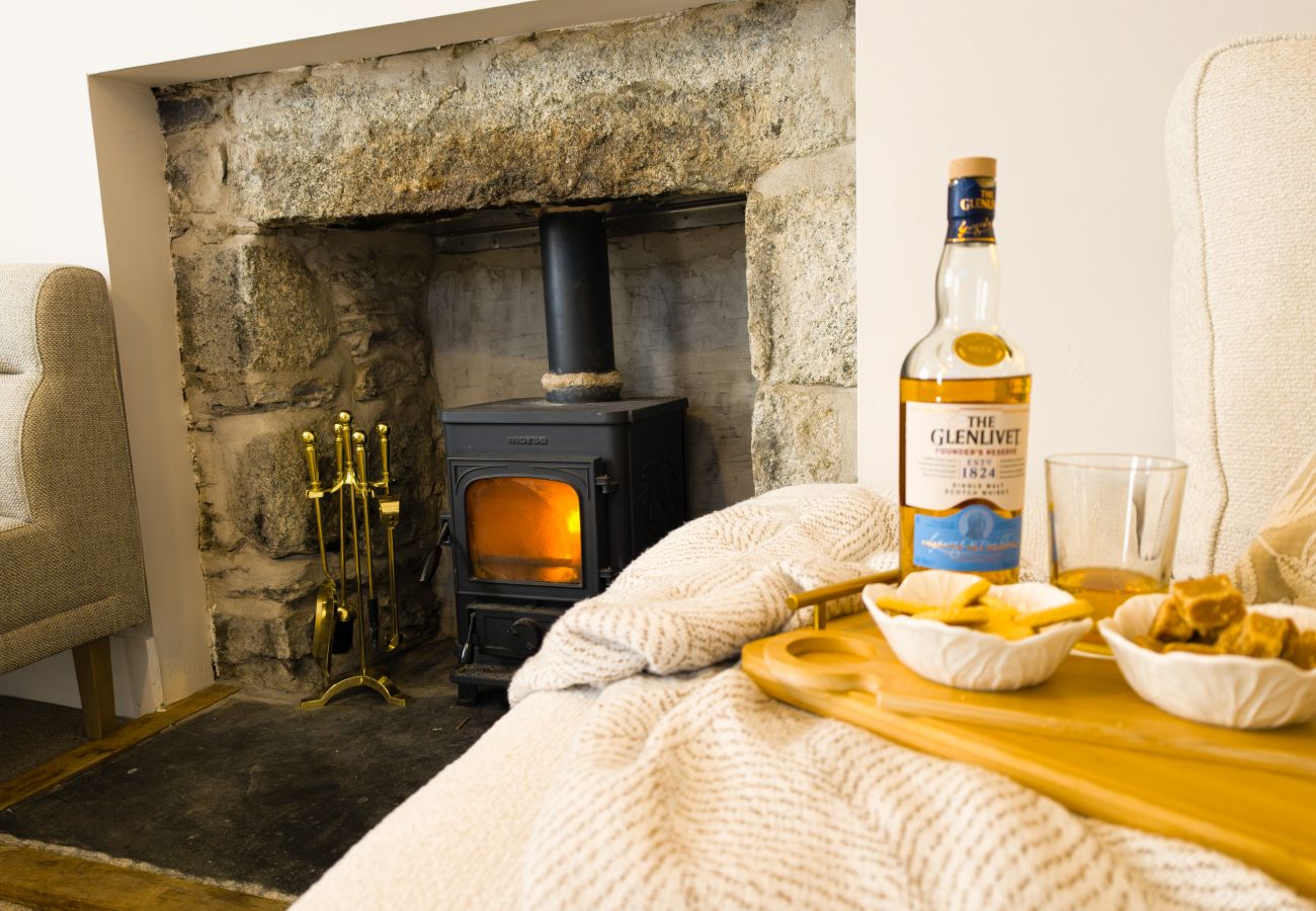 Lit wood burner in a stone fireplace with blanket and whisky at Twinflower, Grantown-on-Spey, Cairngorms