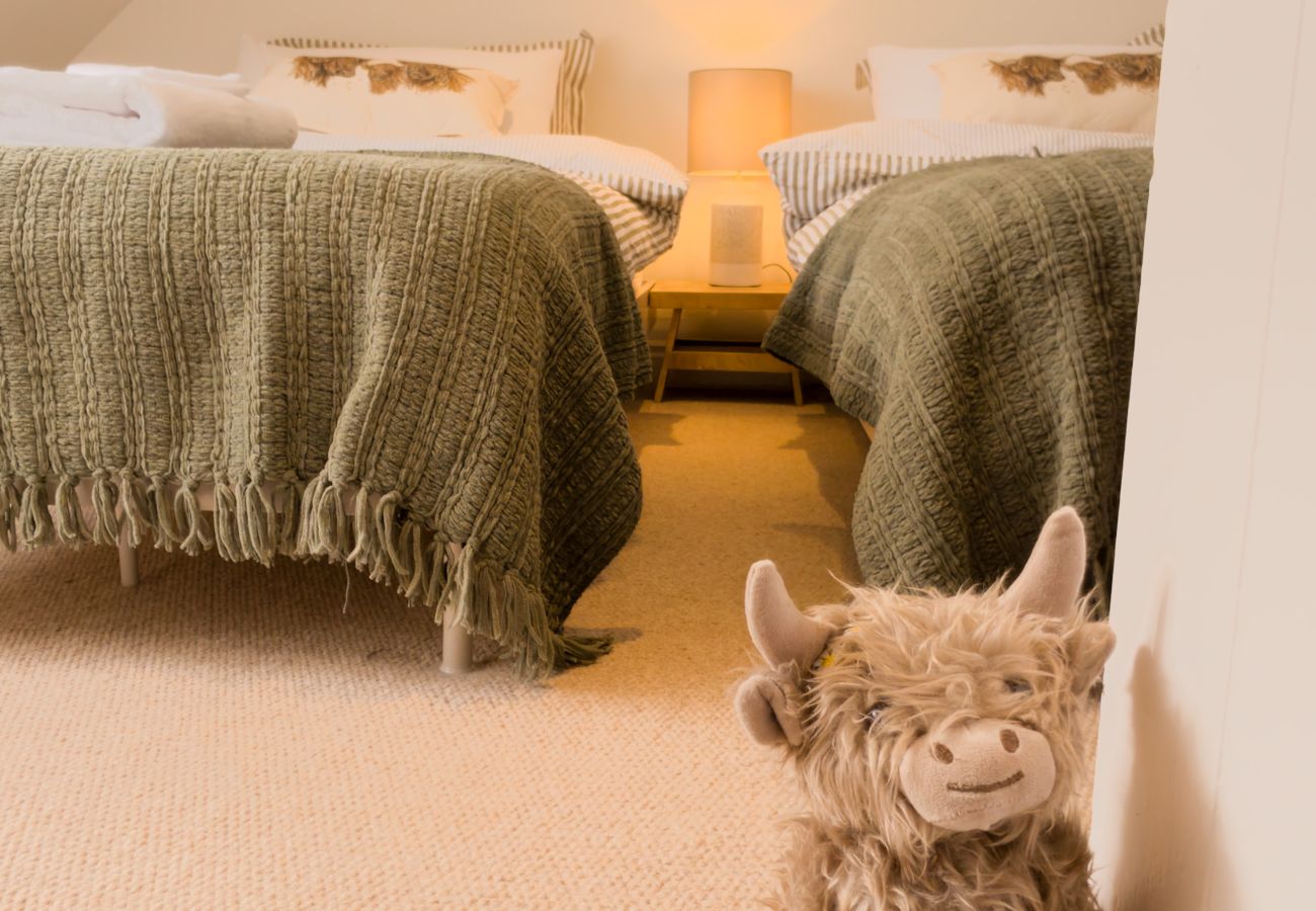 Twin beds with green throws and a Highland cow soft toy at Twinflower, Grantown-on-Spey, Strathspey