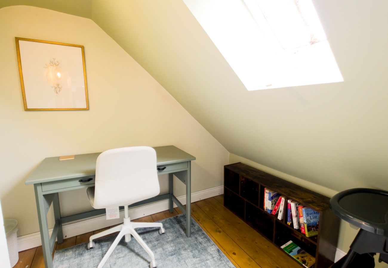 Attic desk under a roof window with a shelf of books and games at Twinflower, Grantown-on-Spey