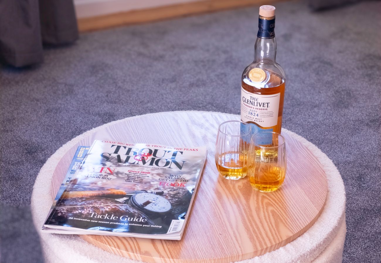Bottle of Speyside single malt with two glasses and a trout and salmon fishing magazine on a round wooden table