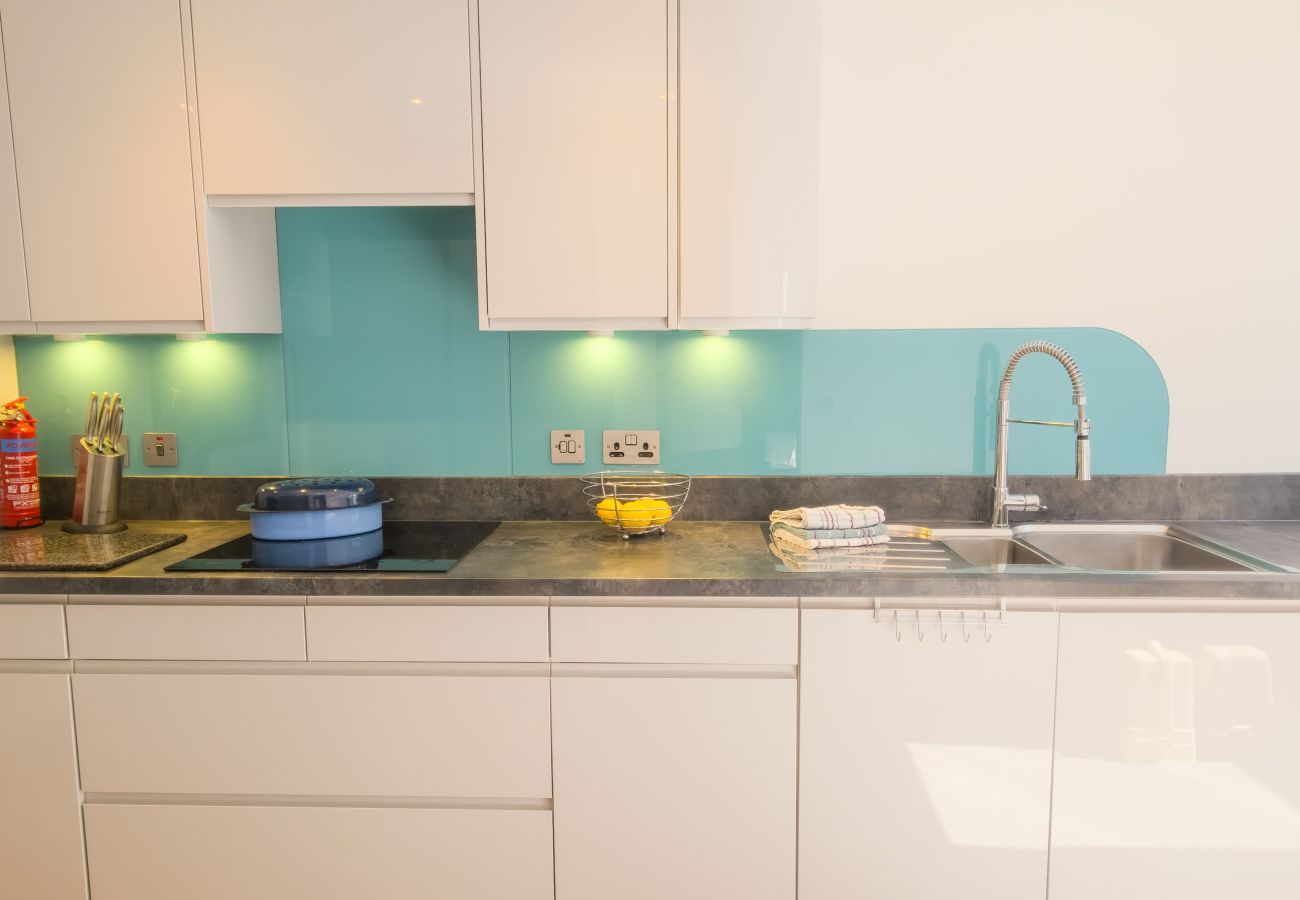 Modern white gloss kitchen with turquoise glass splashback, black glass hob, under-cabinet lights and stainless steel sink