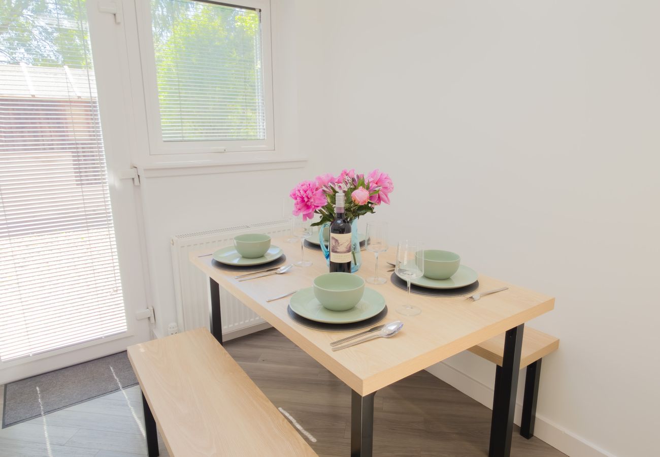 Wooden dining table with bench seating set with sage green plates and bowls and a vase of pink peonies by a window