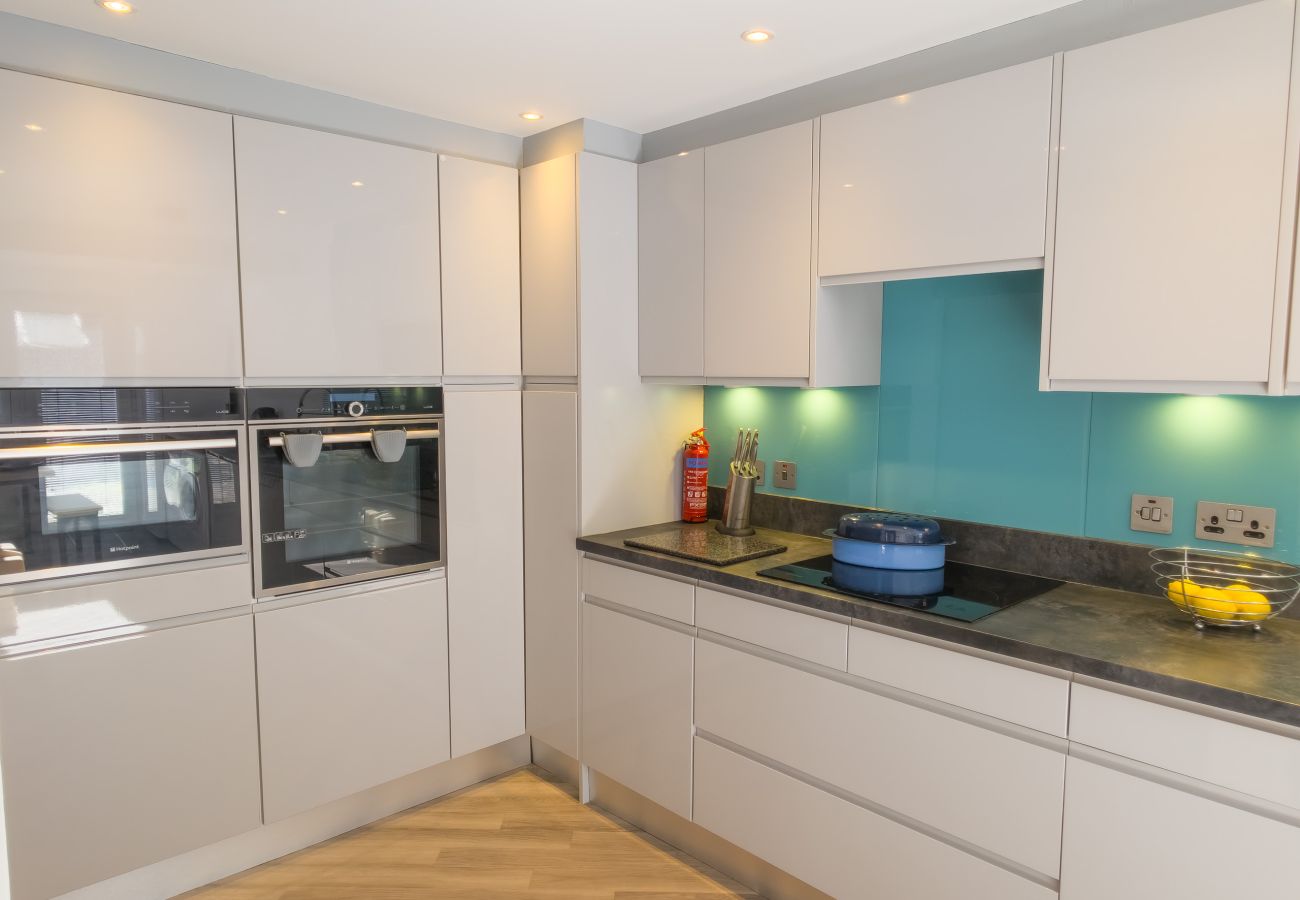 White gloss kitchen with built-in oven and microwave, turquoise splashback and dark worktops
