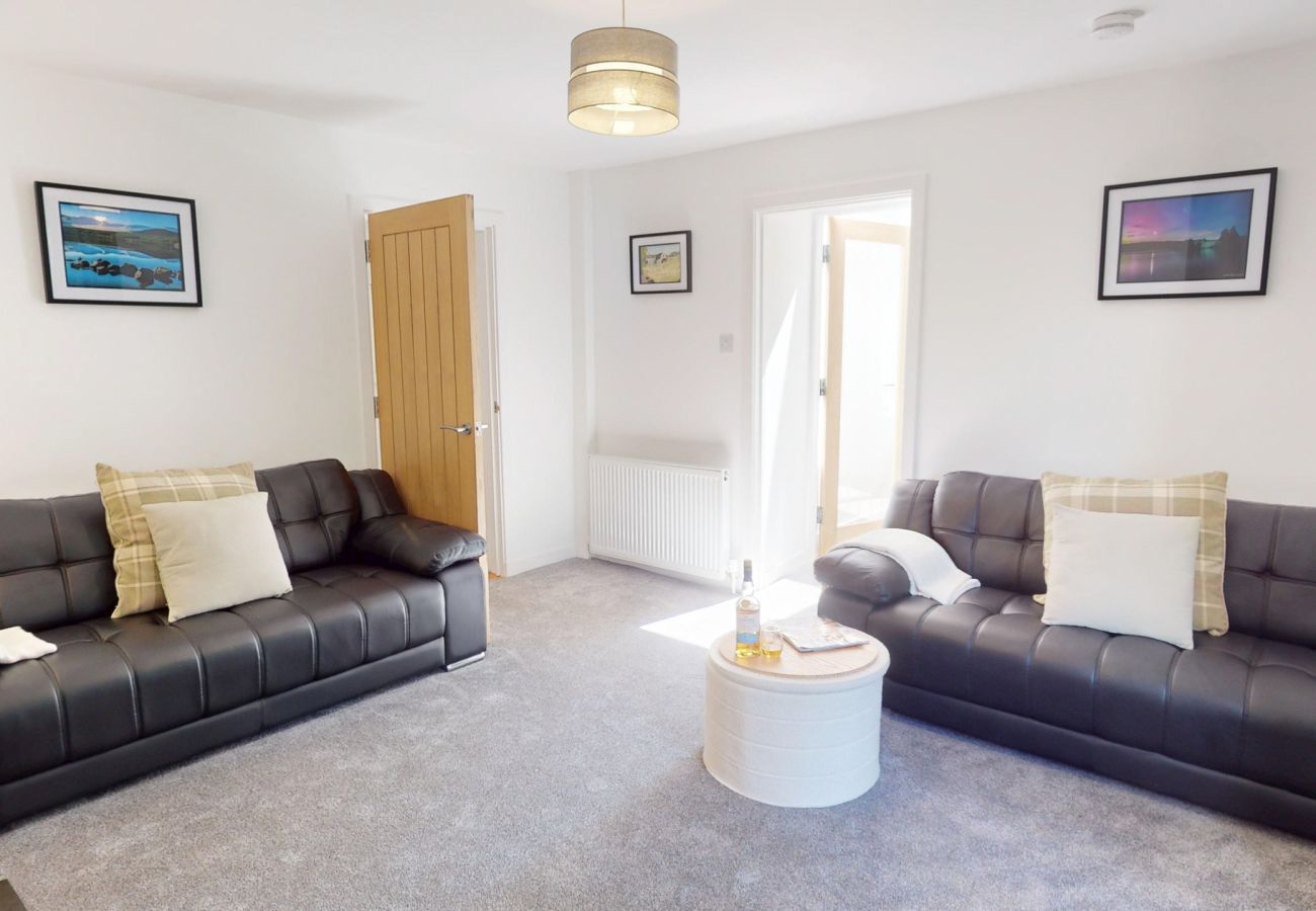 Bright living room with two grey leather sofas, tartan cushions, a round coffee table and Highland landscape prints