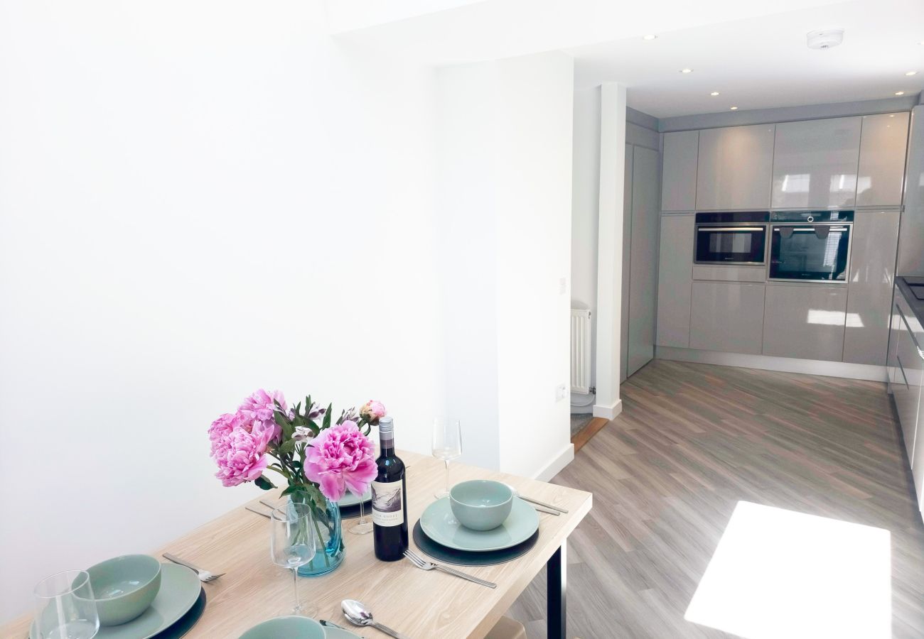 Dining table with peonies and red wine in the foreground, opening onto a modern grey kitchen with built-in ovens