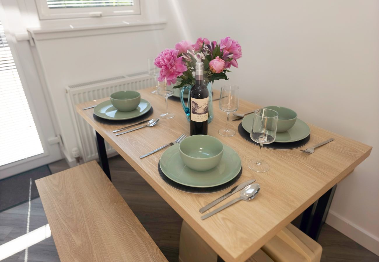 Oak-effect dining table with benches, set with sage green tableware, a bottle of wine and a vase of pink peonies