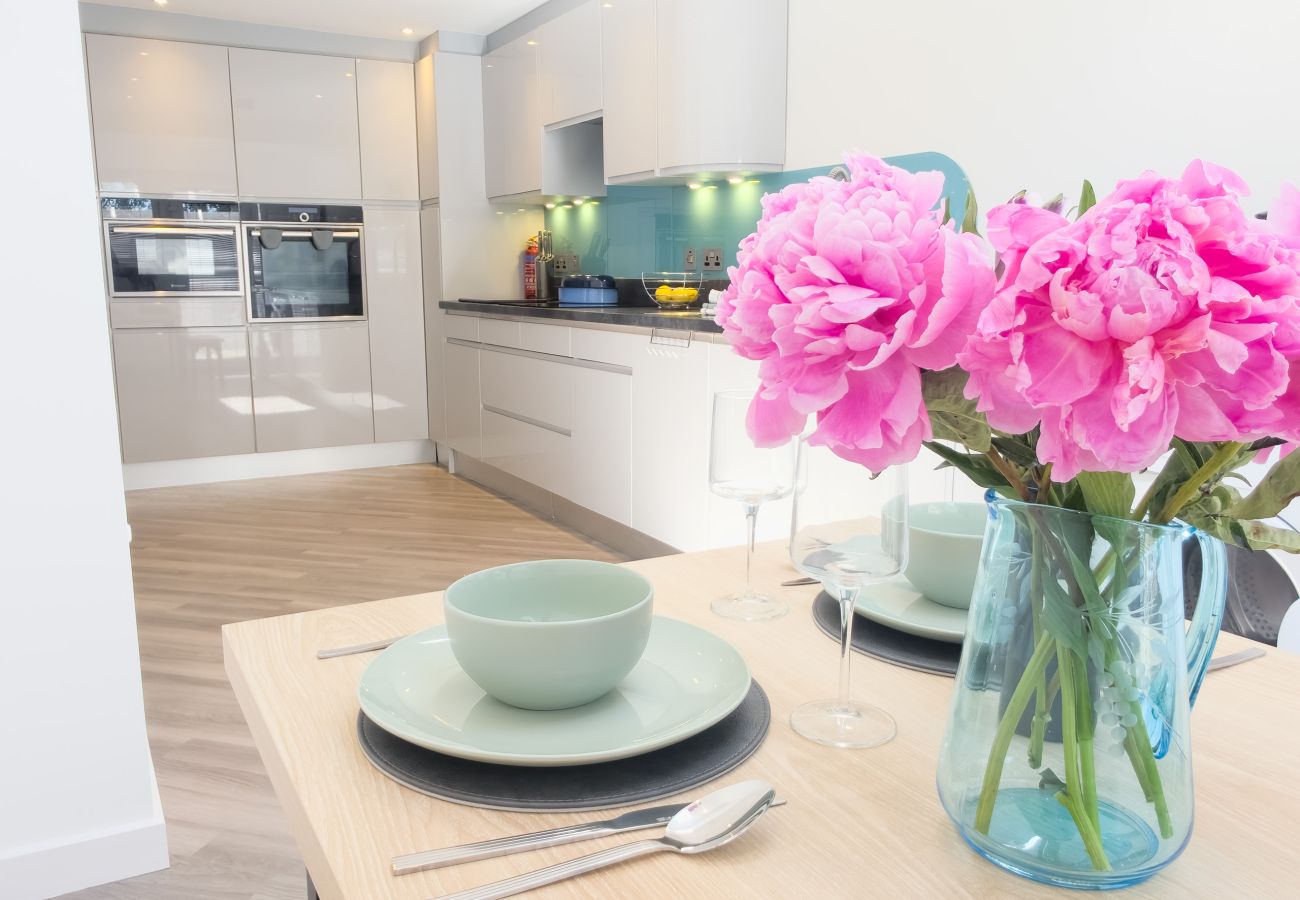 Table set for a family meal with pink peonies in front of a modern white gloss kitchen with built-in ovens