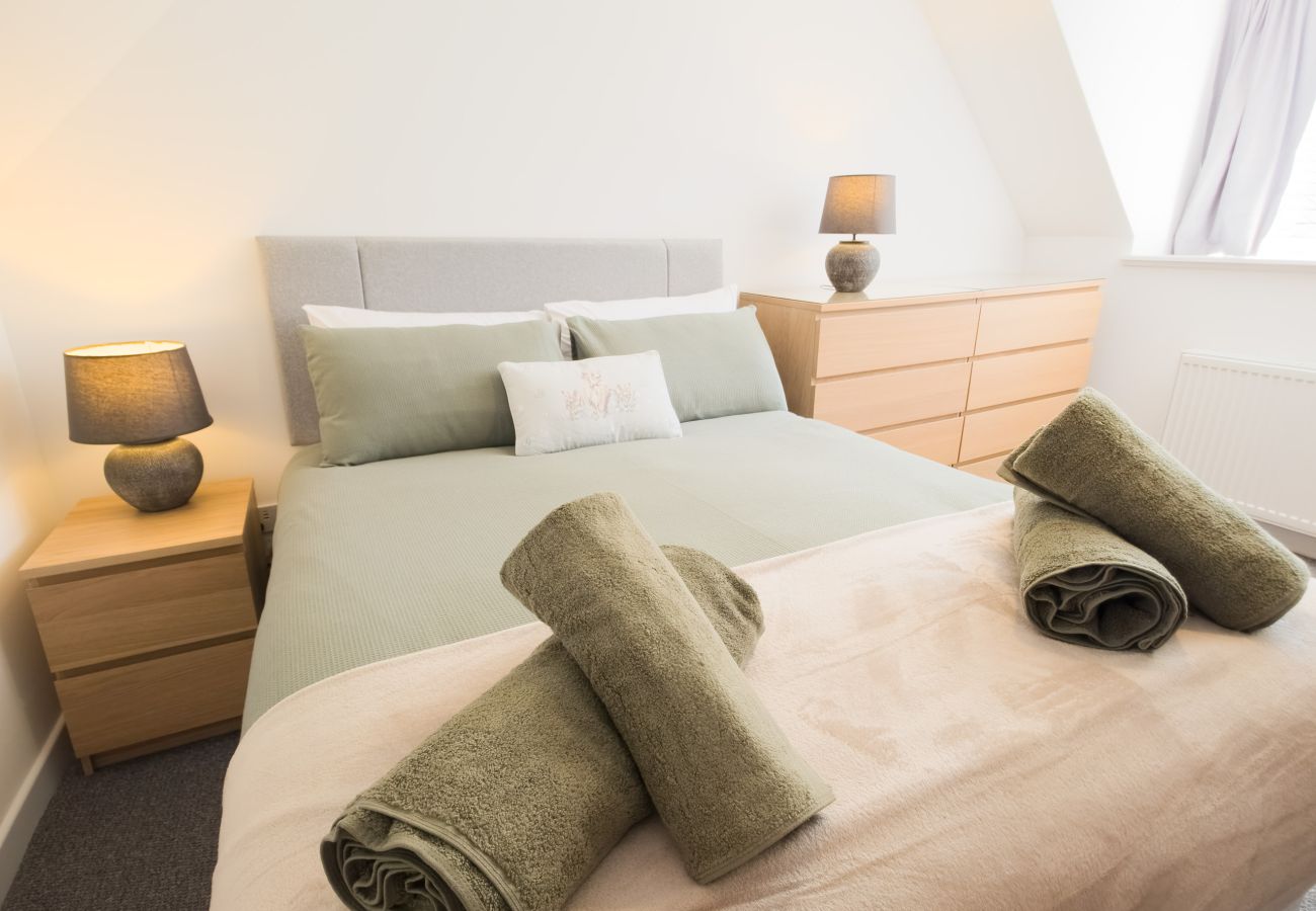 Made-up double bed with green and blush linen, rolled towels, two oak bedside tables and lamps