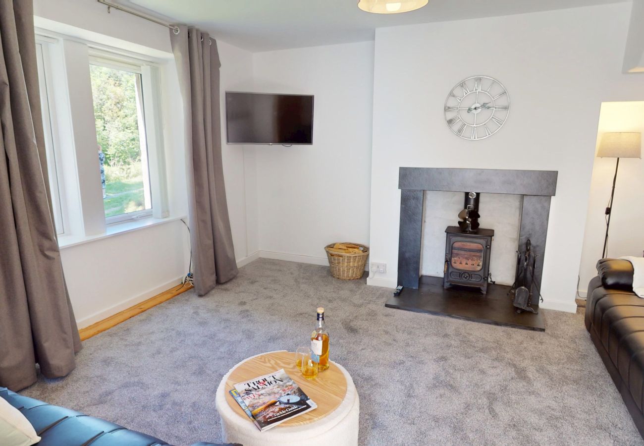 Living room with a wood-burning stove, wall-mounted TV, wall clock and large window with grey curtains