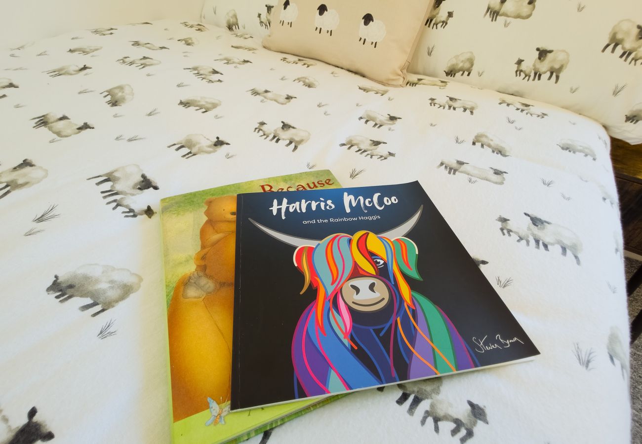 Colourful Highland cow children’s picture book resting on a bed with a sheep-print duvet cover