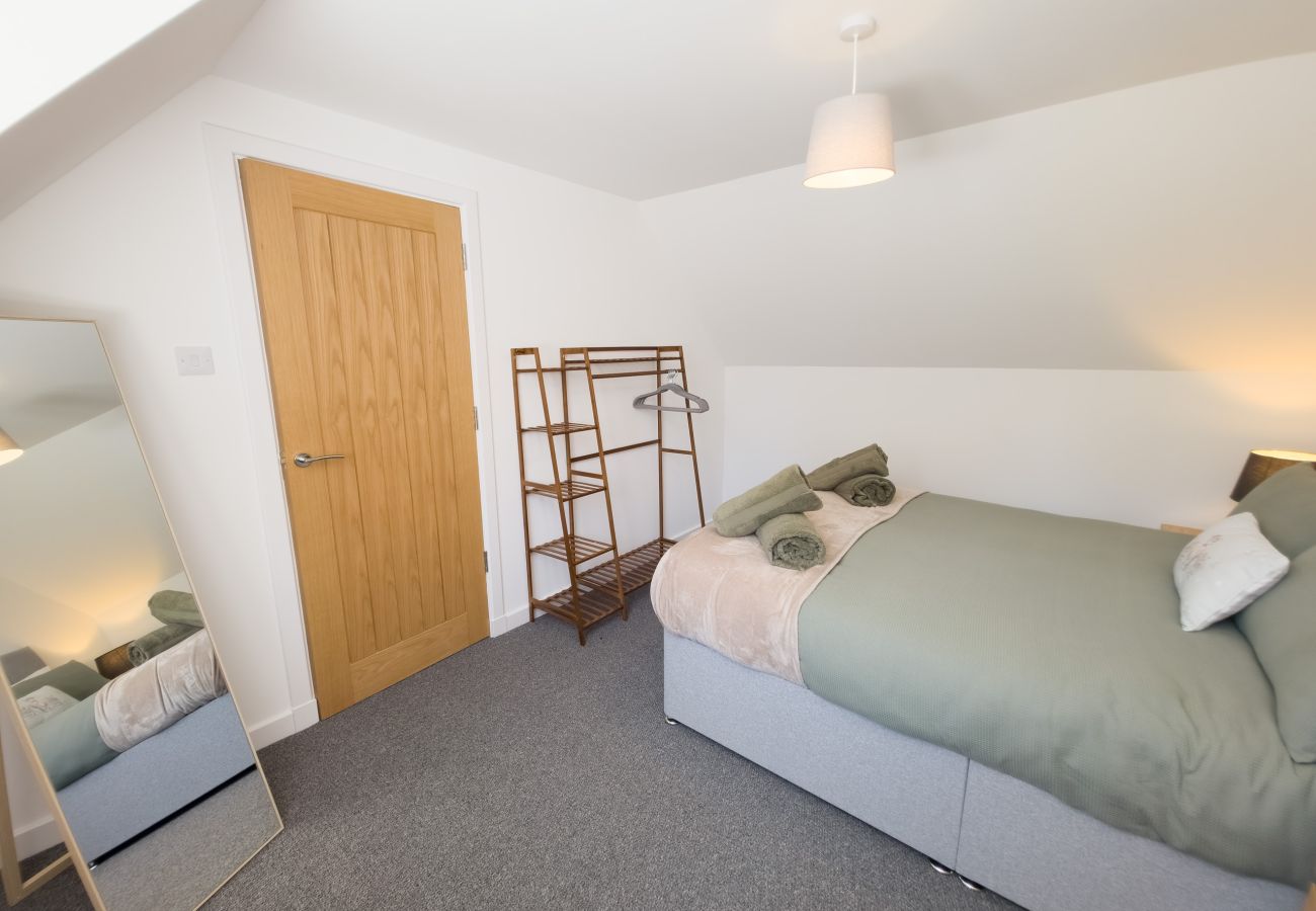 Bright bedroom with a double bed in sage linen, wooden clothes rail, oak door and full-length mirror