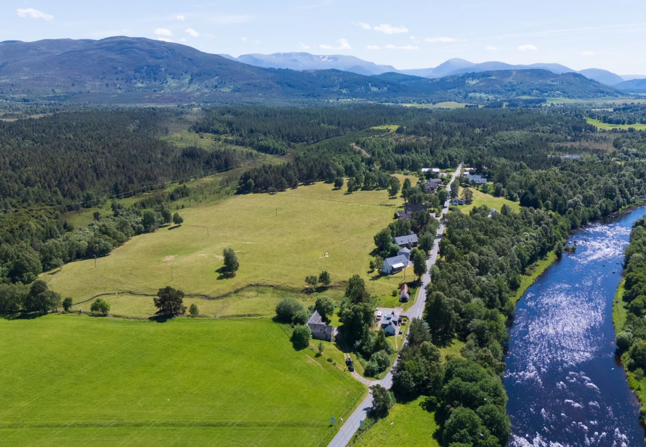 Aerial view of the River Spey flowing past green fields and a small village, with the Cairngorm mountains beyond