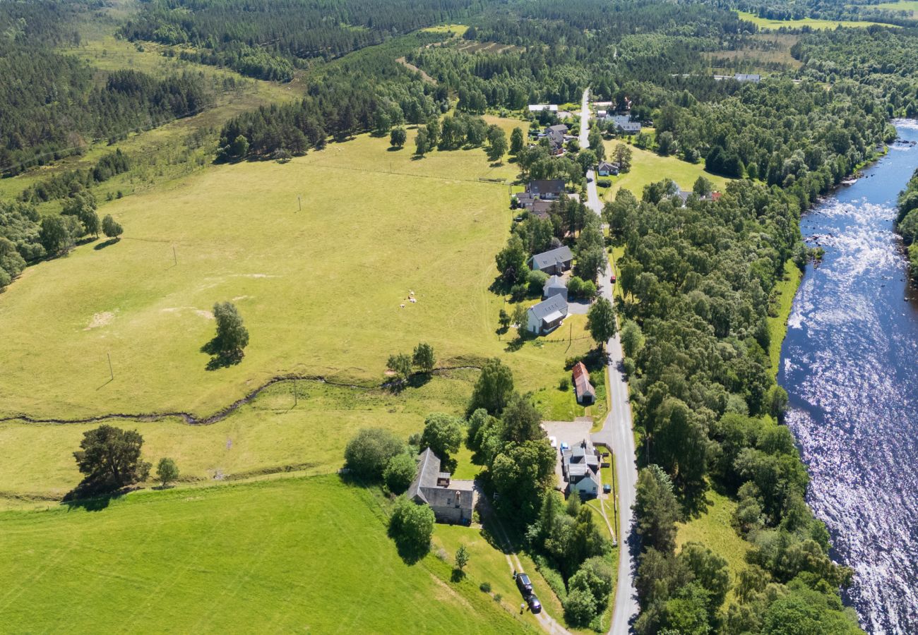 Aerial view of the fast-flowing River Spey beside green fields, woodland and houses along a quiet country road