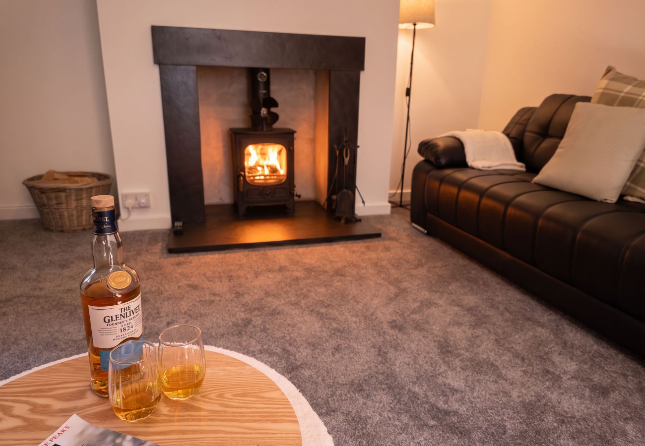 Living room with a lit wood-burning stove, leather sofa, log basket and whisky with two glasses on a side table